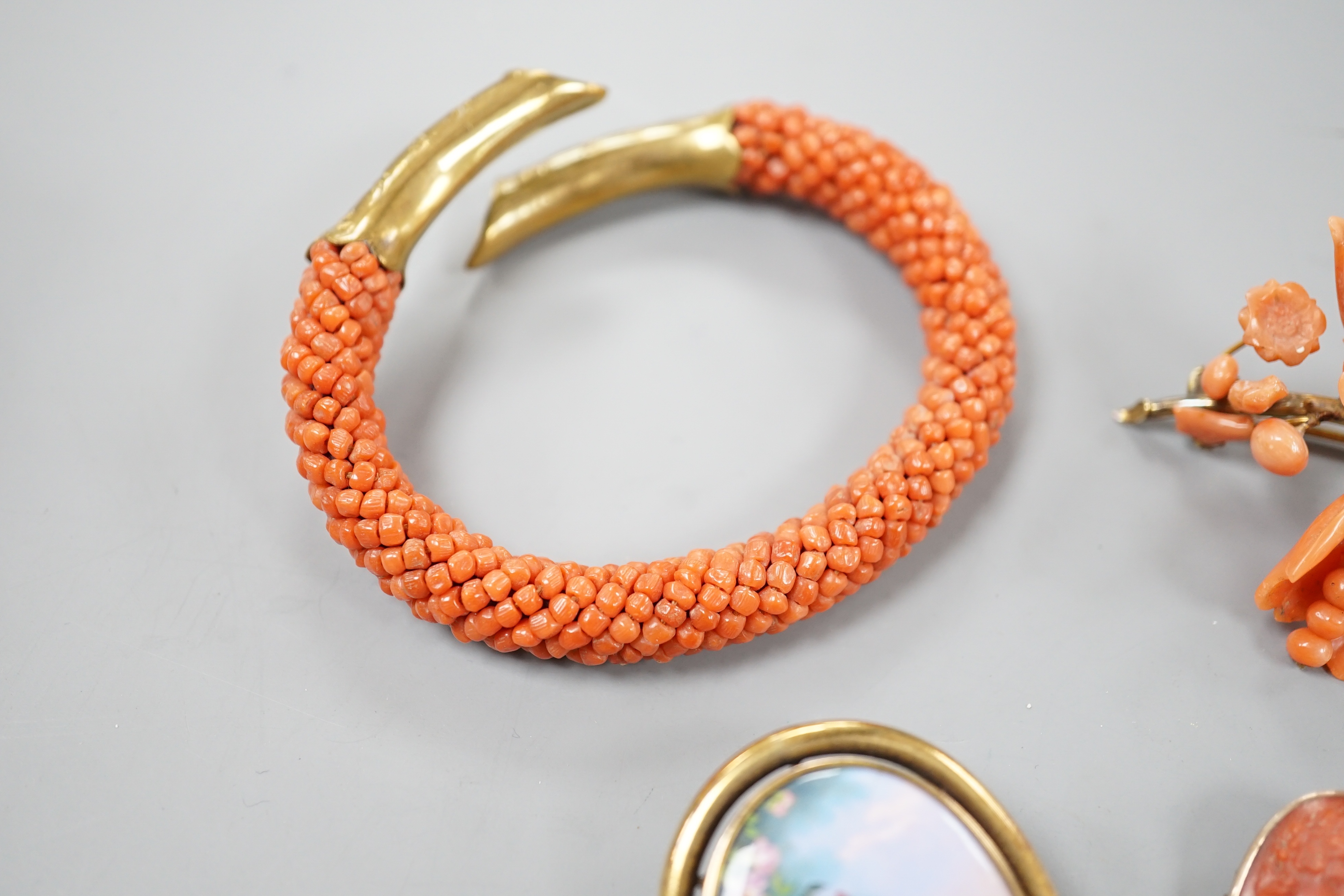 A yellow metal mounted carved coral oval brooch, 30mm, a mounted coral open bangle, a coral brooch and a gilt metal and enamelled brooch.